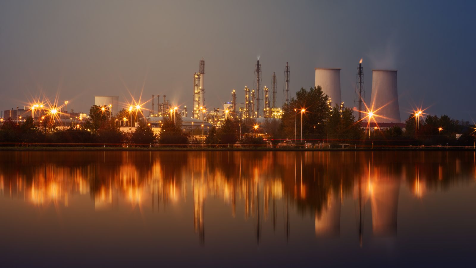 Illuminated gas processing plant reflected in water at dusk